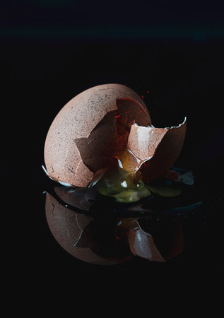 fresh broken egg with yolk sticking out on black background. slight image manipulation