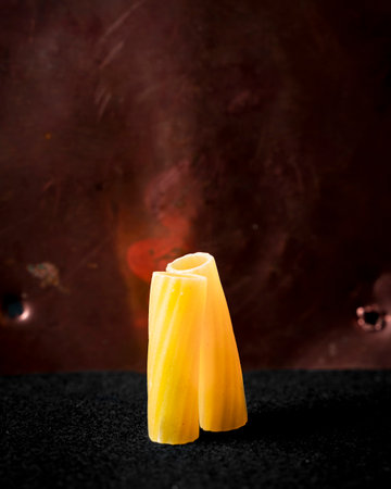 closeup of two macaroni rigati of fresh pasta standing on red metal background