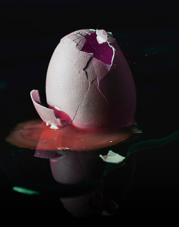fresh broken egg with yolk sticking out on black background. slight image manipulationの写真素材