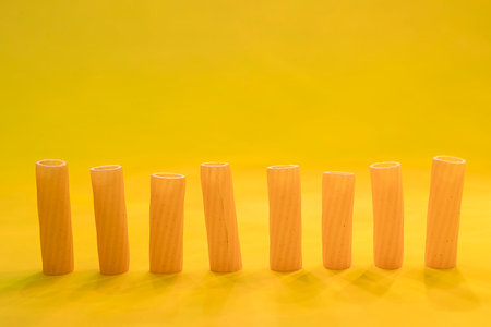 small group of fresh macaroni rigati lined up on yellow background. concept of italian cuisineの写真素材