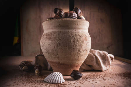 shell shaped chocolates with cream in a clay jar on rough wooden backgroundの写真素材