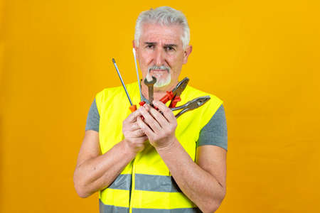 portrait of a mature worker wearing reflector vest showing tools isolated on yellow background