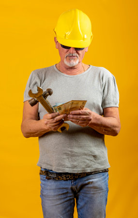 worker with helmet is counting earned euro banknotes on yellow background