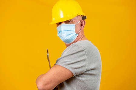 portrait of a worker with yellow helmet and protective mask for covid on yellow backgroundの写真素材