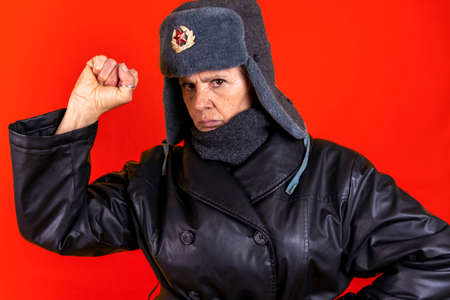 Funny portrait of mature woman. Lady posing dressed as a Russian soldier. Mature woman on colored backgroundsの写真素材
