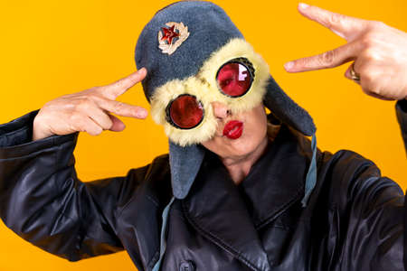 Funny portrait of mature woman. Lady posing dressed as a Russian aviator. Mature woman on colored backgroundsの写真素材