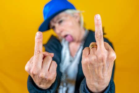 Funny portrait of mature woman. Lady shows the middle finger dressed as an angry rapper. Mature...