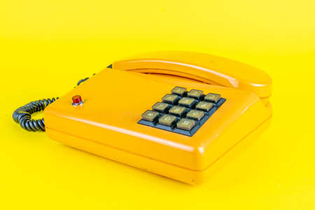 yellow plastic vintage telephone with red button on a yellow background