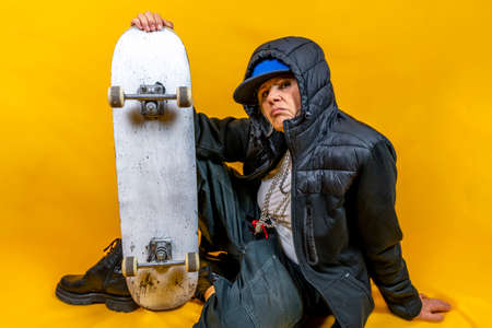 Funny portrait of mature woman. Lady having fun with skate dressed as rapper. Mature woman on...
