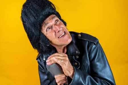 Funny portrait of mature rocker. An old singer dressed in rockabilly style in action. Mature man on colored backgroundsの写真素材