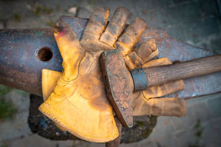 closeup of dirty gloves and hammer over an anvil of blacksmithの写真素材