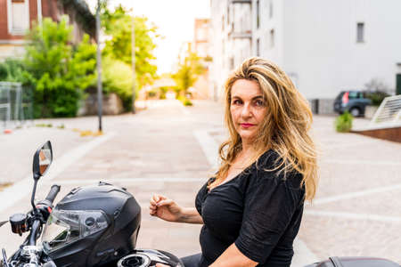 portrait of blonde mature woman with biker helmet sitting on motorcycle outdoorsの写真素材