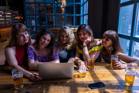 group of beautiful female friends having fun drinking beer and watching computer in a pubの写真素材