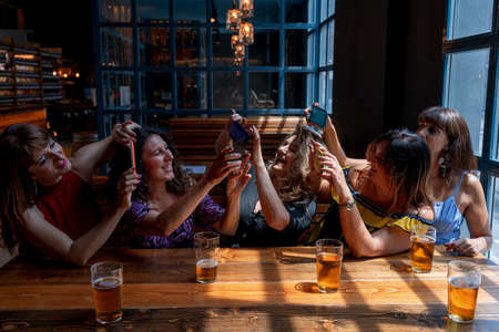 group of smiling female friends take a selfie with a smartphone while drinking beer in a pubの写真素材