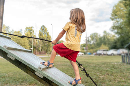 little cute girl is climbing on a wooden plank in an outdoor park