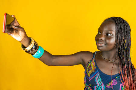 young african female with traditional dress takes a selfie. Studio shot on yellow backgroundの写真素材