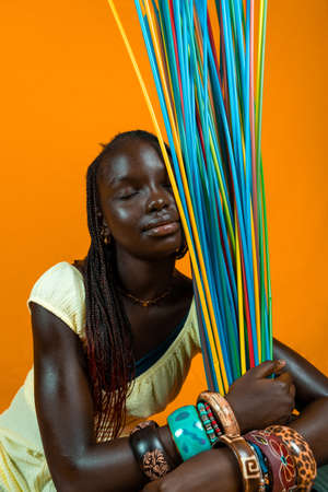young african girl with closed eyes playing with long colorful drinking straws. Studio shot on yellow backgroundの写真素材