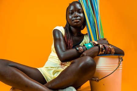 smiling young african teen is playing with long colorful drinking straws. Studio shot on yellow backgroundの写真素材