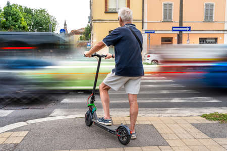 commuter hipster man using electric scooter is waiting to cross a road with heavy traffic. Eco transport conceptの写真素材
