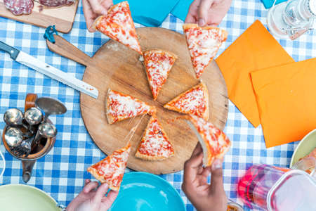 group of friends eating pizza. Top view of four hands taking pizza slices from wooden cutting boardの写真素材