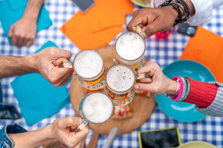 Group of people enjoying and toasting a beer outdoors - Close-up on four pint of beer - Friendship concept with young people having fun togetherの写真素材