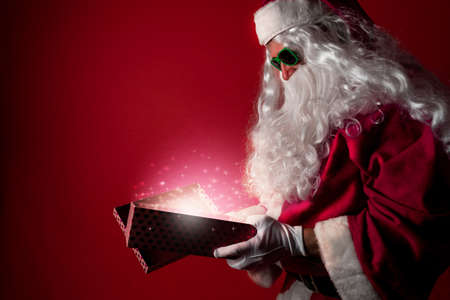 Santa Claus opening a gift box full of Christmas magic dust on a red background - Concept of Christmas moodの写真素材