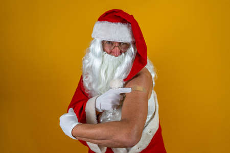 Portrait of happy Santa Claus after having covid-19 vaccination - Santa showing his arm with a bandaid during the Christmas holidays wearing a red capの写真素材