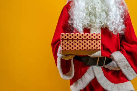 Santa Claus is showing a gift box as a symbol of kindness isolated on orange background - Concept of Christmas atmosphereの写真素材