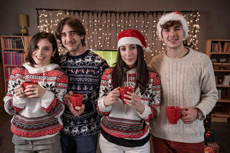 group of four young friends toasting with red cups dressed in red hats and Christmas sweatshirts