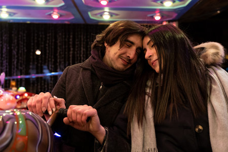 young couple in love have fun on the horses of a carousel full of lights outdoors in winter