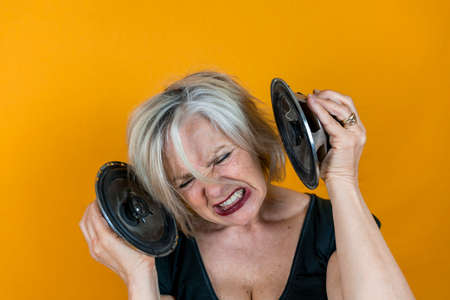 Funny portrait of mature woman. Beautiful lady having fun listening loud music. Mature woman on colored backgroundの写真素材