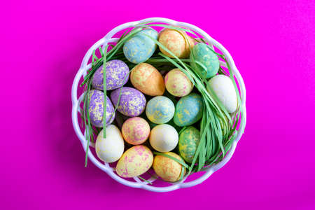 group of decorative easter eggs inside a basket on fuchsia background - top view