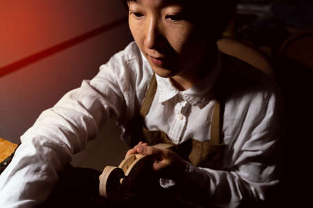 young Chinese female violin maker working on the neck of the violin under construction in her...