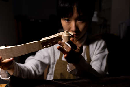 young Chinese female violin maker working on the neck of the violin under construction in her workshopの写真素材