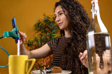beautiful curly haired woman is chatting with the smartphone hanging on a phone holder having...