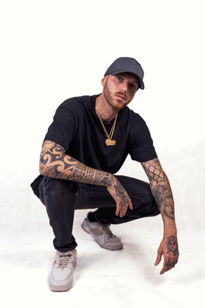 tattooed rap singer posing in studio wearing black clothes on a white background