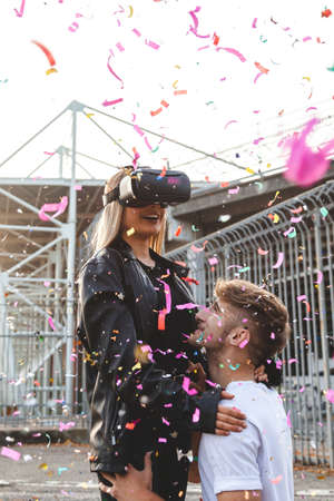 beautiful couple in love having fun in a rain of colorful confetti with virtual reality glasses. concept of technology addictionの写真素材