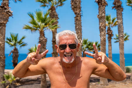 portrait of attractive middle aged man wearing sunglasses making victory sign with hands with...
