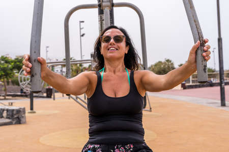 attractive middle aged woman doing gymnastic exercises in an outdoor public gym at a seaside resort