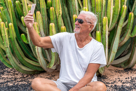 handsome middle-aged man takes a selfie in front of a large cactus in an exotic seaside resort - summer vacation conceptの写真素材