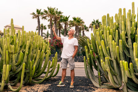 handsome middle-aged man takes a selfie in front of a large cactus in an exotic seaside resort - summer vacation conceptの写真素材