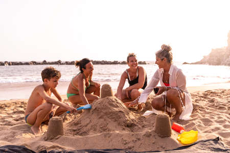 family on vacation playing with sand castles on the beach at sunset - summer vacation conceptの写真素材