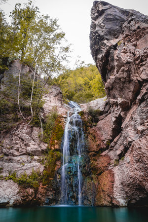 wonderful small waterfall that forms a pond of emerald water in an autumn forest