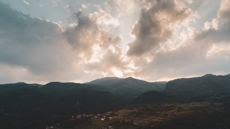 panoramic view of a valley surrounded by hills at sunset with the sun obscured by cloudsの写真素材