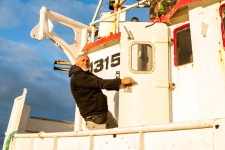 Middle-aged man playing captain on a boat stranded on an Icelandic beach in the midnight sunの写真素材