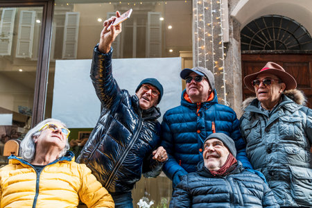 group of happy retired mature men taking a selfie with smart phone on the street in winterの写真素材