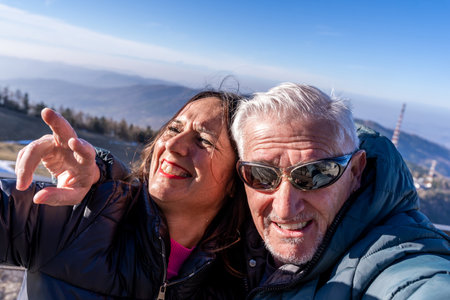 middle aged couple wearing winter clothes taking a selfie over a mountain - concept of happy people on vacationの写真素材