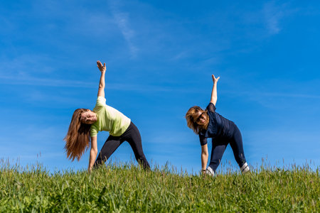 couple of pretty athletic women doing gymnastics exercises outdoors - wellness conceptの写真素材