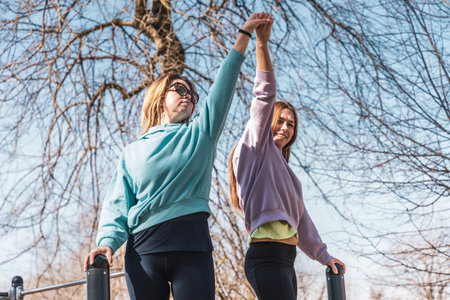 couple of female athletes having fun while climbing on sport metal structure outdoors - wellness conceptの写真素材