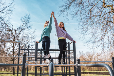 couple of female athletes having fun while climbing on sport metal structure outdoors - wellness conceptの写真素材